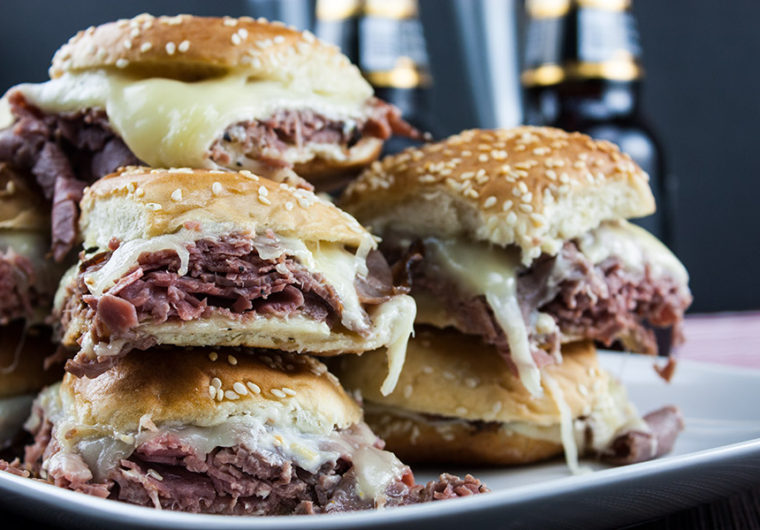 sliders stacked on white plate beer bottles in background