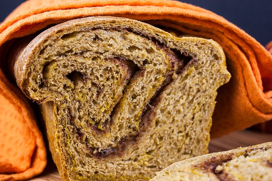 Pumpkin Cinnamon Swirl Bread loaf cut to show cross section covered with an orange towel.