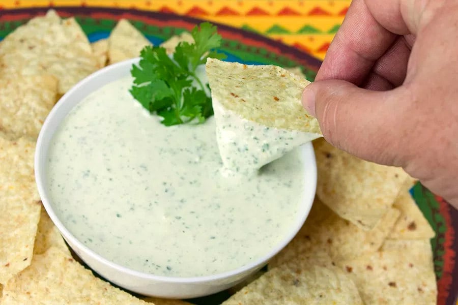 Creamy Jalapeno Cilantro Dip in a white bowl with a tortilla chip being dipped in