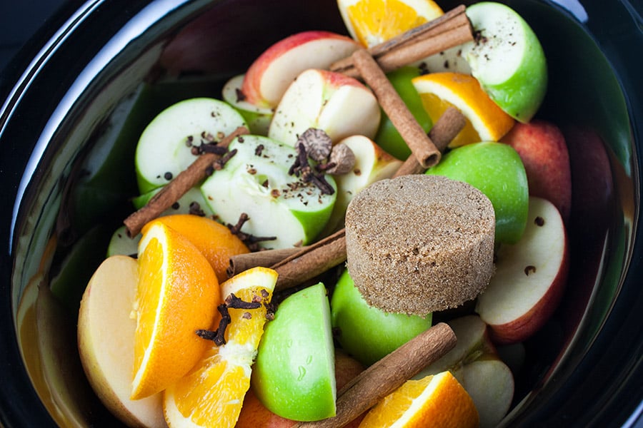 Apples, orange, cinnamon sticks and spices in the crock of a slow cooker.