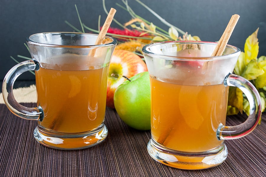 Slow Cooker Apple Cider in glass mugs with cinnamon sticks.