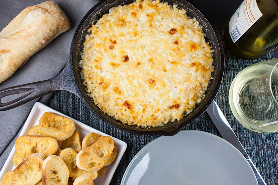 Baked Vidalia Onion Dip in a cast iron skillet with toasted baguette slices on a white platter