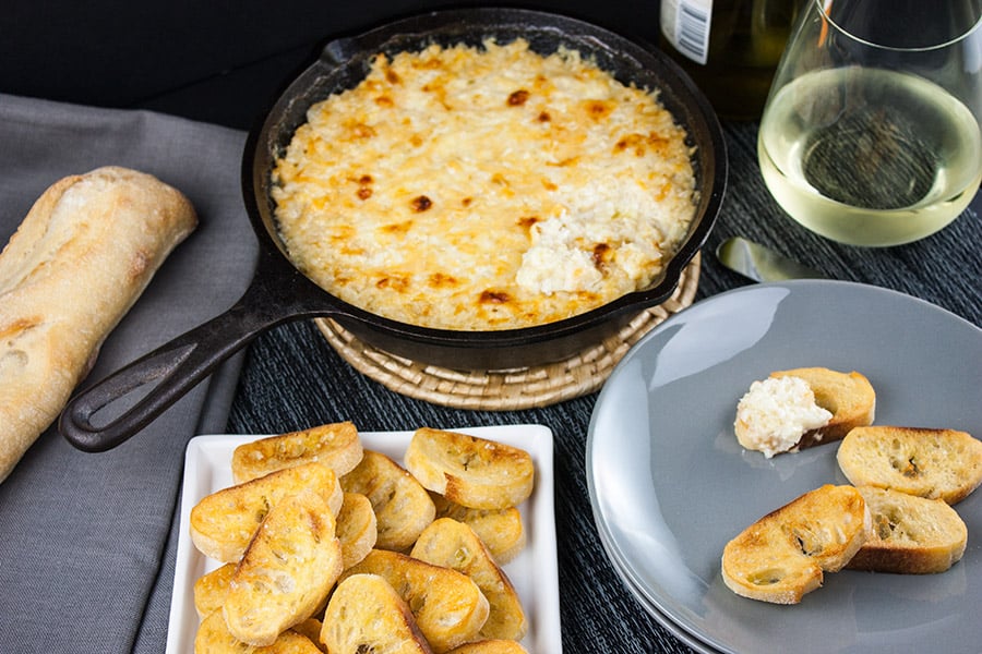 Baked Vidalia Onion Dip in a cast iron skillet with toasted baguette slice on a gray plate