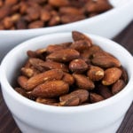 Roasted salted almonds in a white bowl.