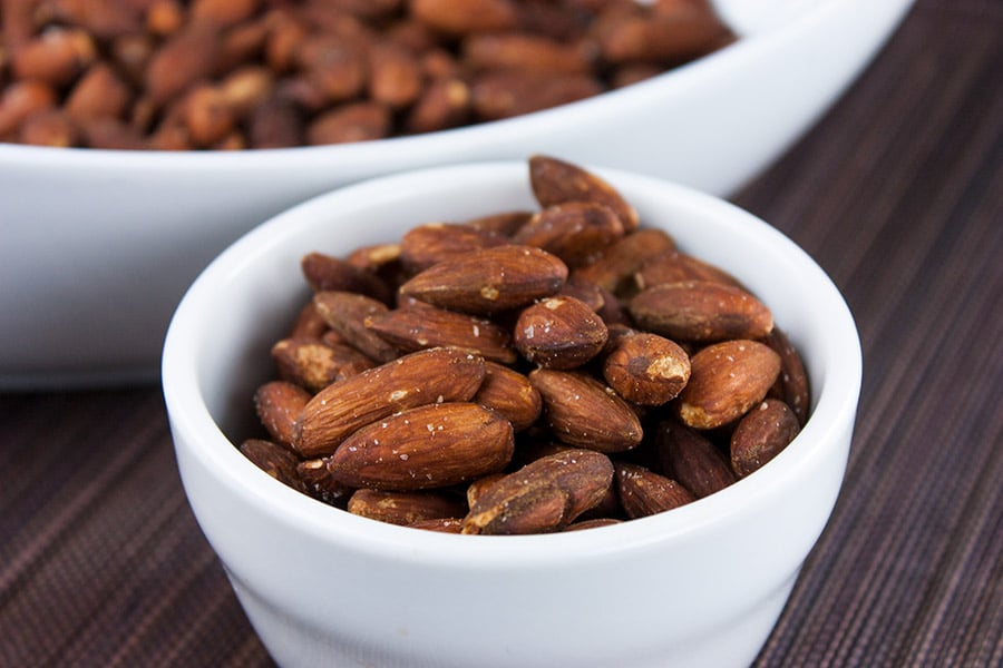 Roasted salted almonds in a white bowl.