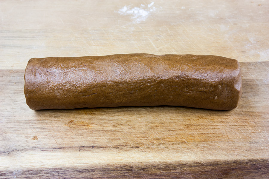 Crispy Gingersnap Cookies dough rolled into a log on a wooden cutting board