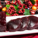 Cranberry sauce sliced on a white tray with berries in the background.