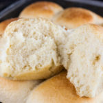 One roll cut open lying on the pan of dinner rolls.