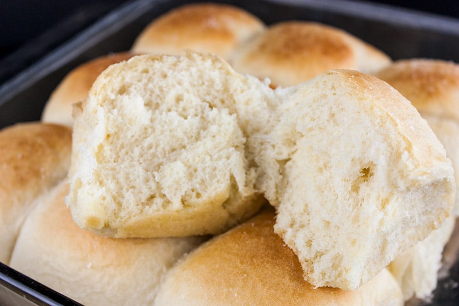 One roll cut open lying on the pan of dinner rolls.