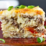 A slice of sausage hashbrown breakfast casserole on a red plate garnished with green onions.