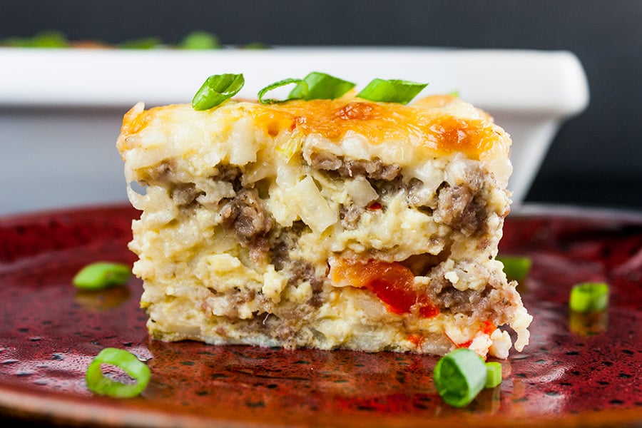 A serving of sausage hashbrown casserole on a plate garnished with diced green onions.