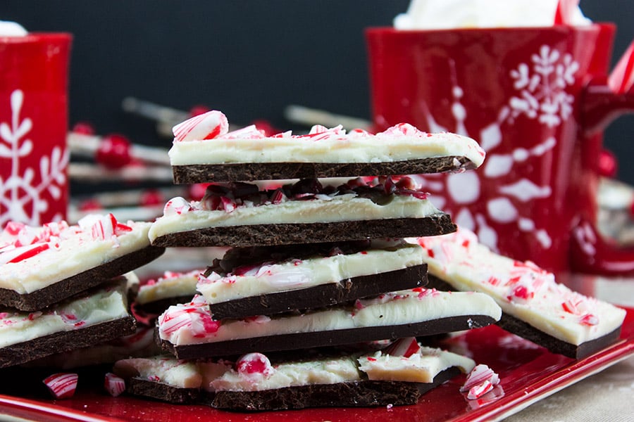 Dark chocolate peppermint bark stacked on a plate with Christmas coffee mugs in the background.