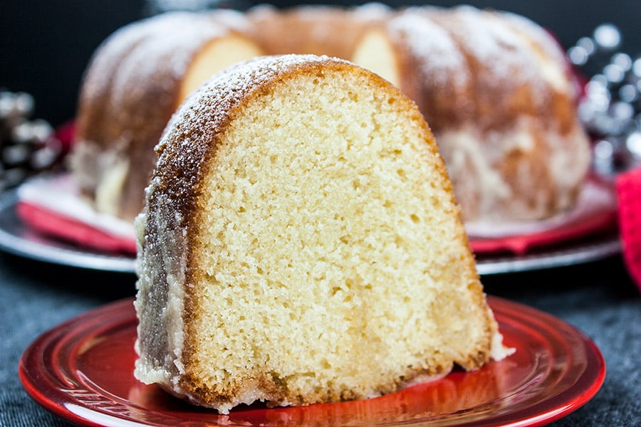 A slice of the eggnog bundt cake on a small red plate with the whole cake in the background.