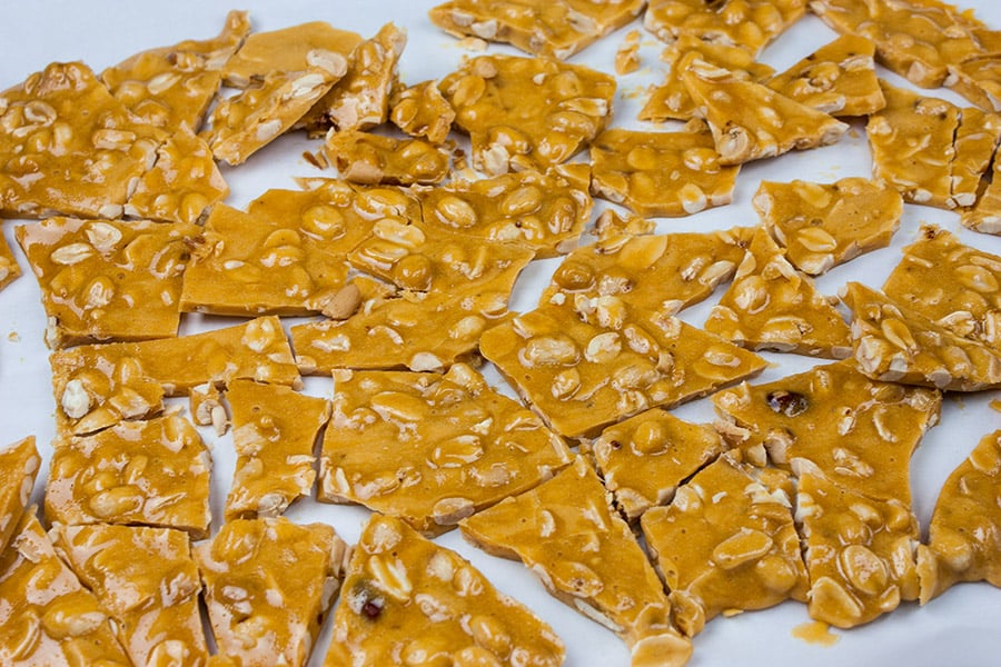 Peanut brittle broken into pieces on parchment paper.