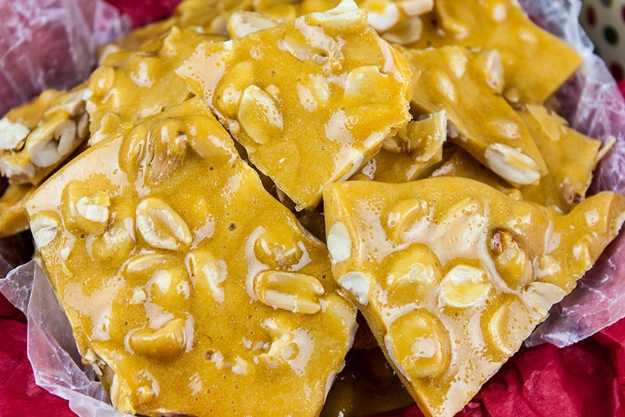 Peanut brittle stacked in a tin lined with red tissue paper.