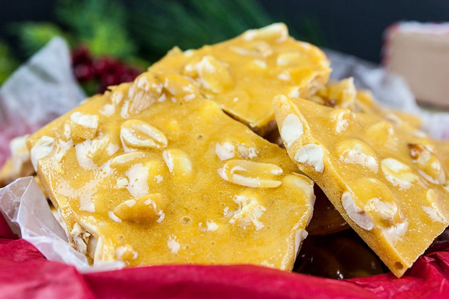 Peanut brittle stacked in a tin lined with red tissue paper.