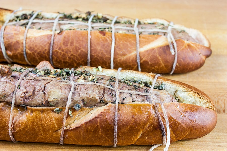 Tucan Pork Tenderloin - Pork tenderloin smothered in fresh herbs roasted inside a crusty baguette on a wooden cutting board