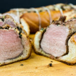 Tuscan pork tenderloin sliced on wooden cutting board.