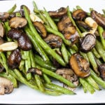 Roasted green beans and mushrooms on a white serving platter.