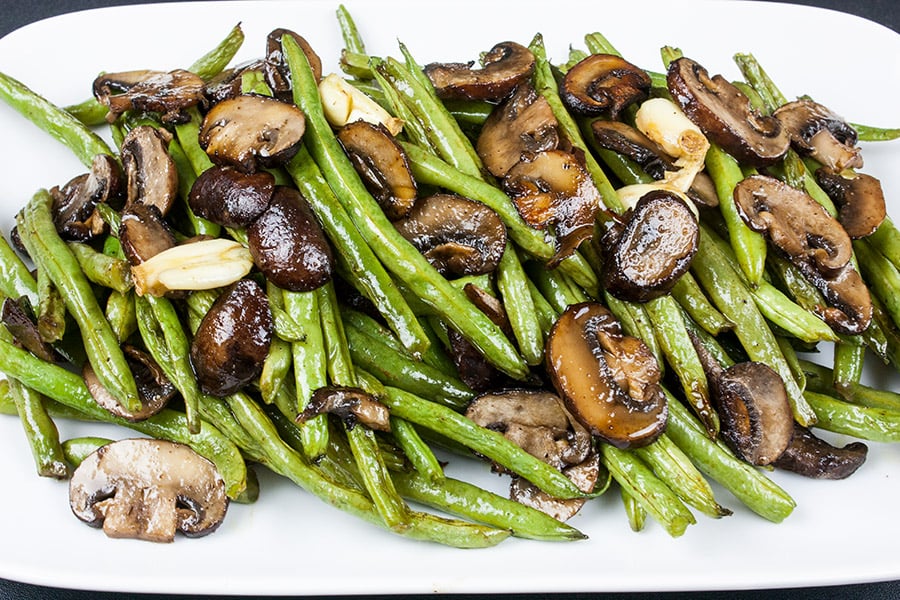 Roasted green beans and mushrooms on a white serving platter.