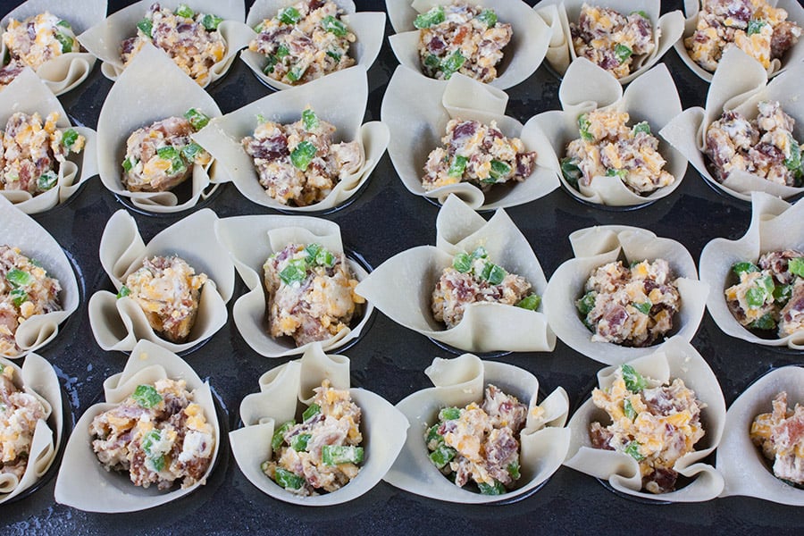 wonton wrappers filled with jalapeno popper filling in a mini muffin pan.