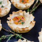 Close up of pepper jelly brie bite on slate with fresh thyme sprig garnish.