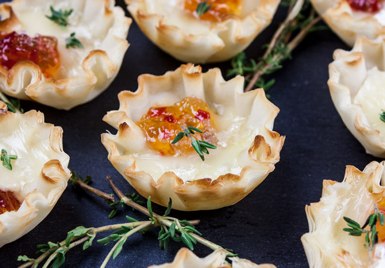 close up of pepper jelly brie bite on slate with fresh thyme sprig garnish
