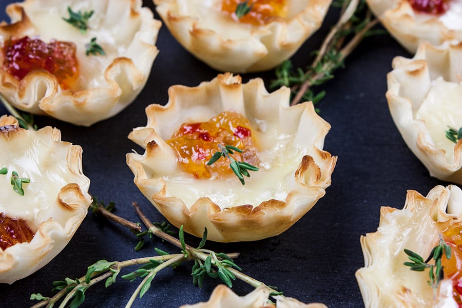 Close up of pepper jelly brie bite on slate with fresh thyme sprig garnish.