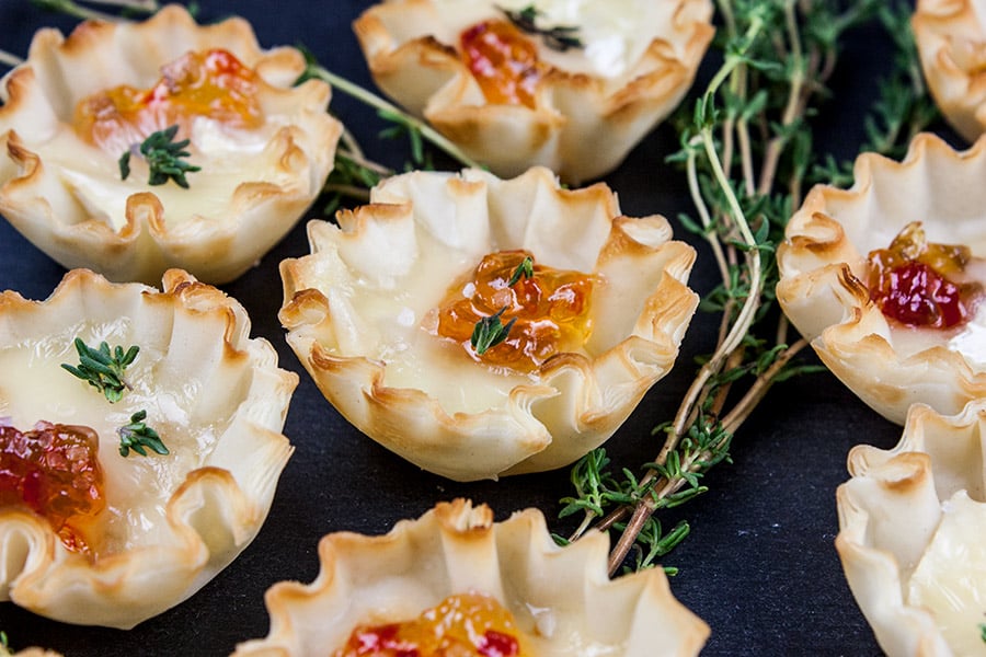 closeup of Pepper Jelly Brie Bites on a black slate garnished with fresh thyme