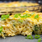 Slice of crustless broccoli cheddar quiche on gray plate garnished with diced green onions.