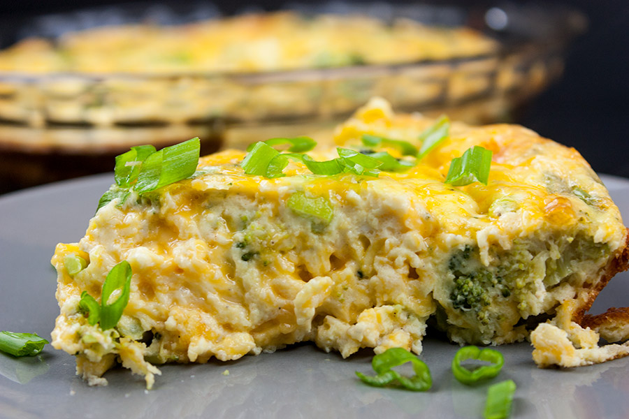 Slice of crustless broccoli cheddar quiche on gray plate garnished with diced green onions.