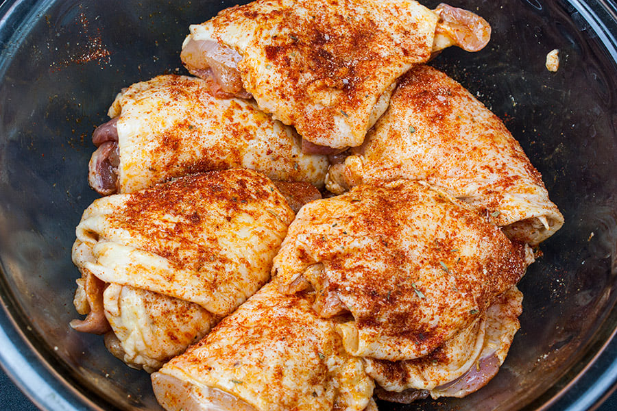 Raw chicken thighs in a glass bowl covered in seasonings