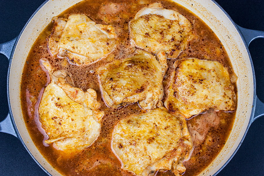 Spanish Chicken thighs seared in skillet with rice and broth added.