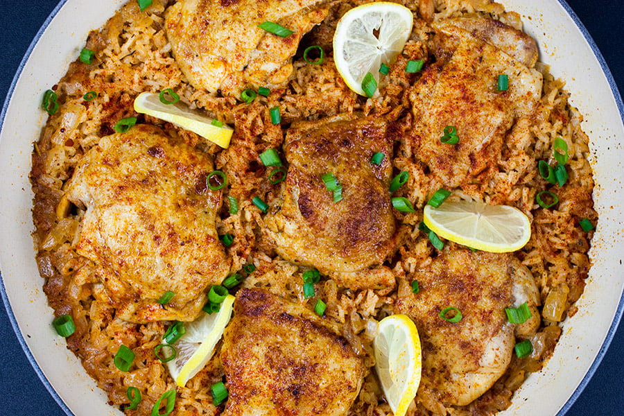 One Pan Spanish chicken and rice cooked in the skillet garnished with lemons slices and green onions.