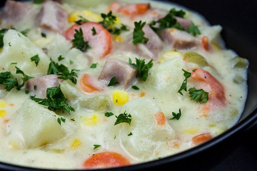 Easy Ham and Potato Soup in a dark bowl garnished with chopped parsley.