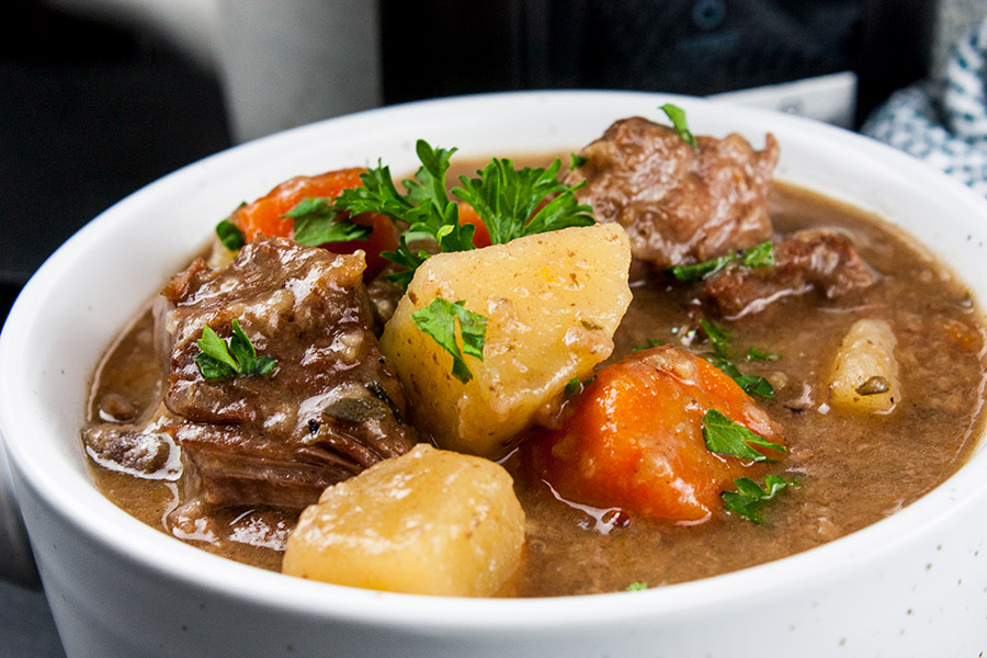 Beef stew in a white bowl garnished with chopped parsley.