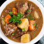 Slow cooker beef stew in a white bowl garnished with chopped parsley.