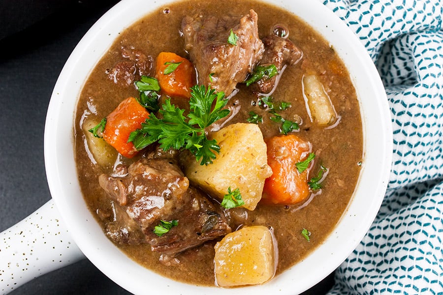 Slow cooker beef stew in a white bowl garnished with chopped parsley.