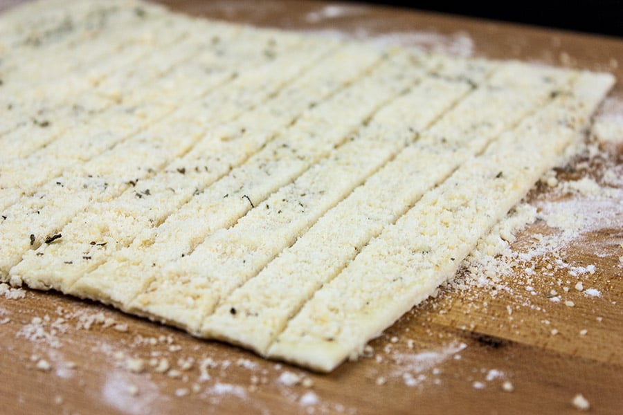 Dough rolled out on cutting board sprinkled with cheese and herbs.