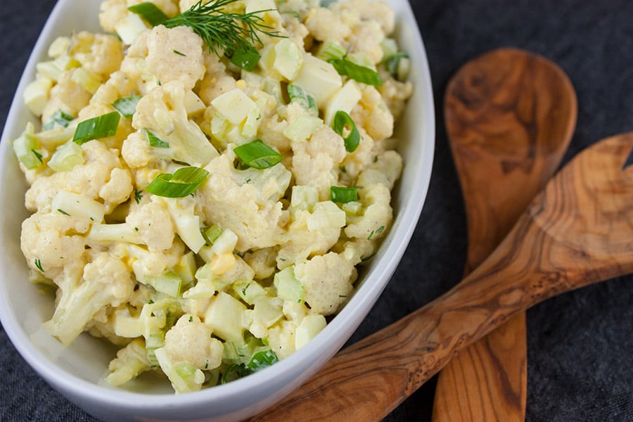 Cauliflower Mock Potato Salad in a white serving bowl with wooden serving spoons
