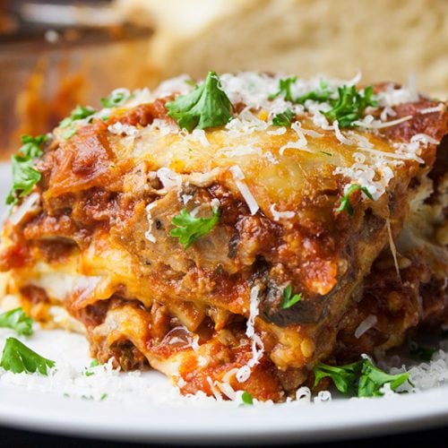 Lasagna on a white plate garnished with parsley and cheese.