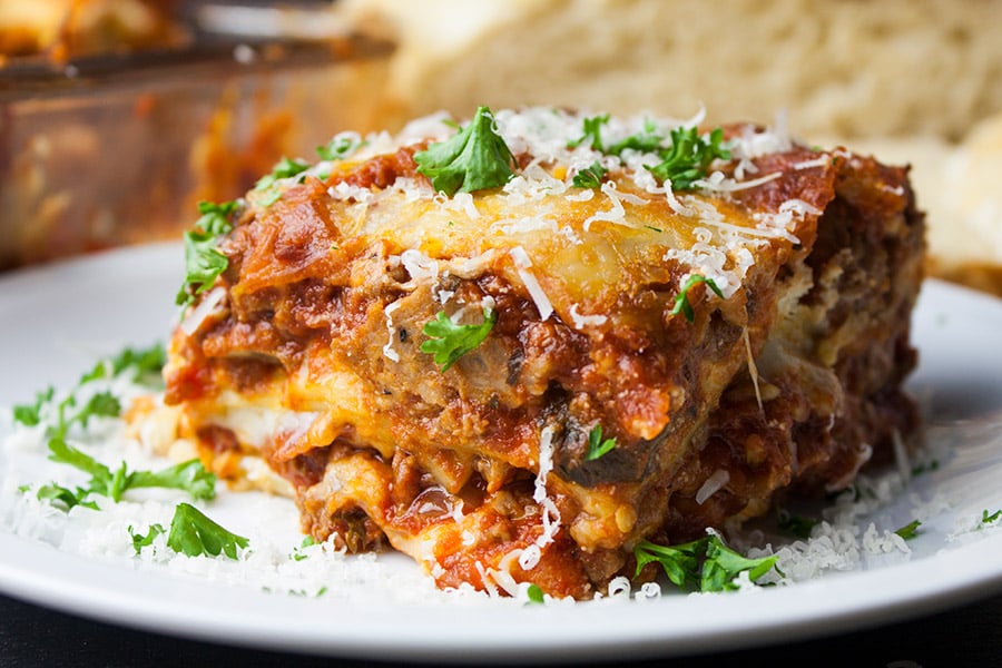 Lasagna on a white plate garnished with parsley and cheese.