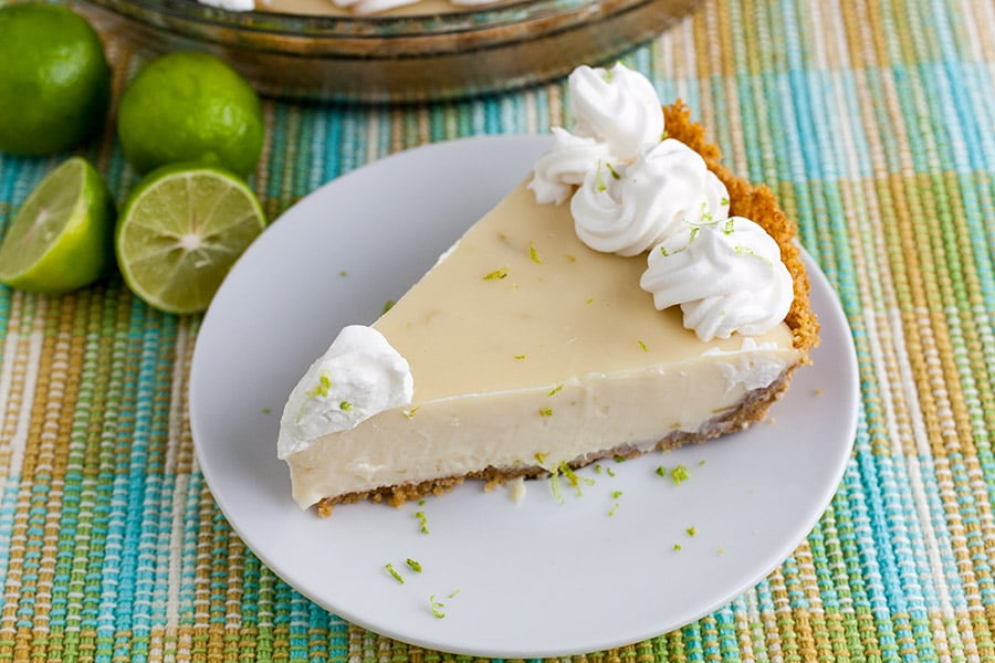A slice of Key lime pie on a light plate garnished with whipped cream and lime zest.