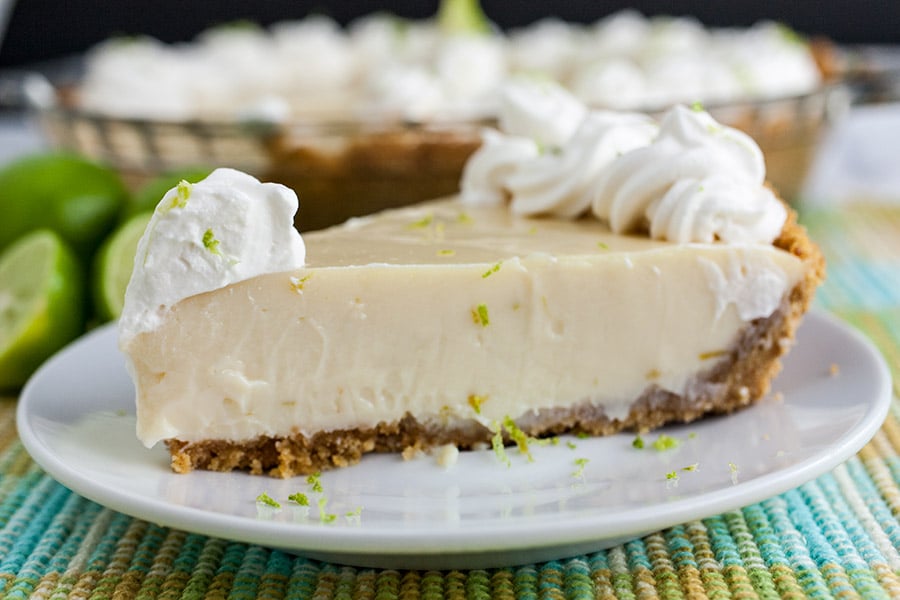 A slice of Key lime pie on a light plate garnished with whipped cream and lime zest.