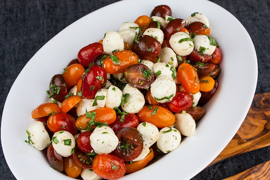 Fresh Tomato Mozzarella Salad in a white oval bowl with wooden spoons