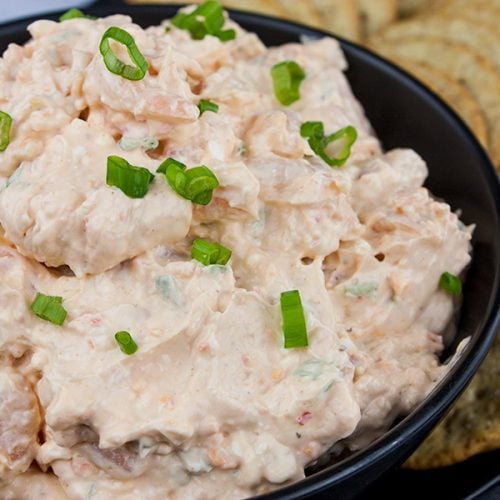 Easy cold shrimp dip in a black bowl garnished with diced green onions and surrounded by crackers.