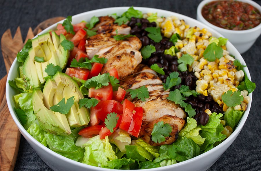 Southwest Grilled Chicken Salad in a large white serving platter with wooden spoons and a ramekin of salsa
