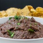 Easy Black Bean Dip in a white bowl with tortilla chips in the distance.