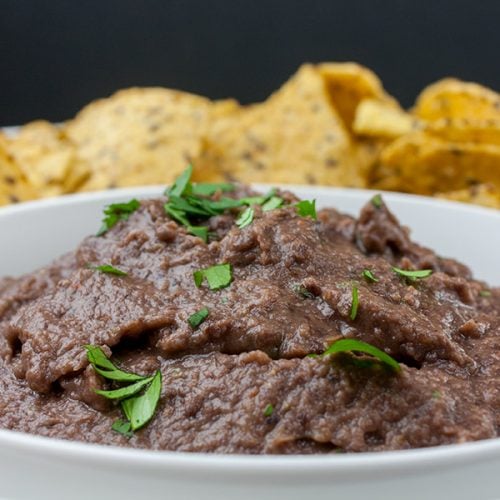 Easy Black Bean Dip in a white bowl with tortilla chips in the distance.