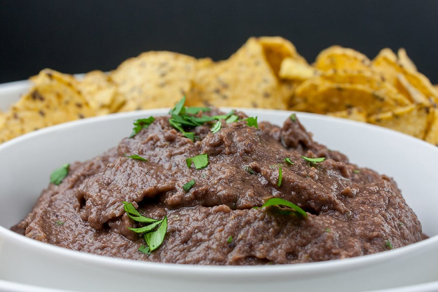 Easy Black Bean Dip in a white bowl with tortilla chips in the distance.